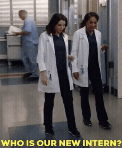 Two Female Doctors Are Walking Down A Hallway With The Words " Who Is Our New Intern " Behind Them GIF
