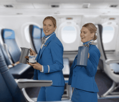 Two Female Flight Attendants In Blue Uniforms Smiling Holding Pitchers GIF