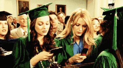 Two Female Graduates Looking At Cell Phones GIF