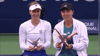 Two Female Tennis Players Holding Trophies In Front Of A Sign That Says Que GIF