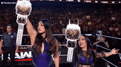 two female wrestlers hold up their belts in front of a crowd