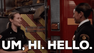 Two Firefighters Are Standing Next To Each Other In Front Of A Fire Truck And Talking To Each Other . GIF