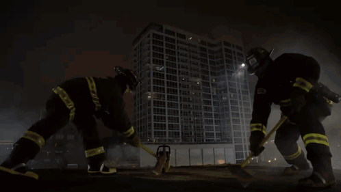 Two Firefighters In Front Of Building With Hammer And Chainsaw GIF