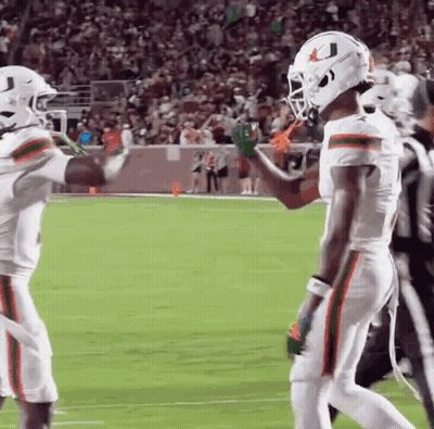 Two Football Players Are Giving Each Other High Fives On The Field . GIF