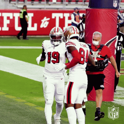 Two Football Players Are Hugging Each Other On A Field With The Nfl Logo In The Background GIF