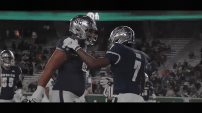 Two Football Players Are Hugging Each Other On The Field GIF