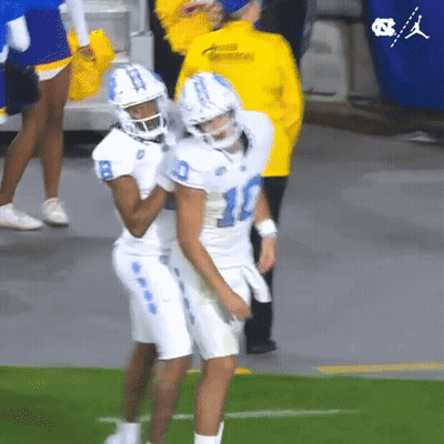 Two Football Players Are Hugging Each Other On The Field While A Cheerleader Stands Behind Them . GIF