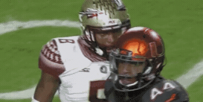 Two Football Players Are Standing Next To Each Other On A Field . One Of The Players Is Wearing A Helmet . GIF