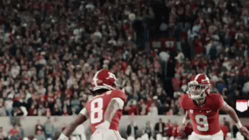 Two Football Players Wearing Red Uniforms With The Number 8 And 9 GIF