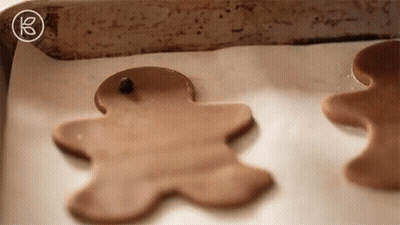Two Gingerbread Men Are Sitting On A Baking Sheet On Top Of A Piece Of Wax Paper . GIF