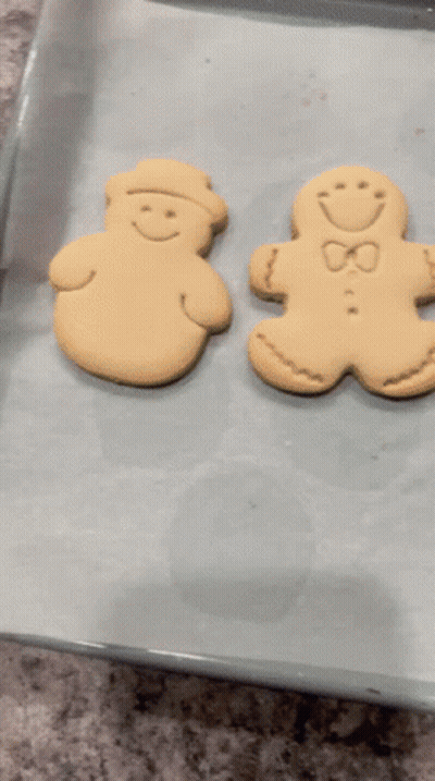 Two Gingerbread Men Are Sitting On A Baking Sheet On Top Of Wax Paper GIF