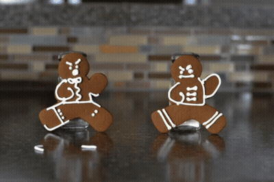 Two Gingerbread Men Standing Next To A Salt Shaker On A Counter GIF