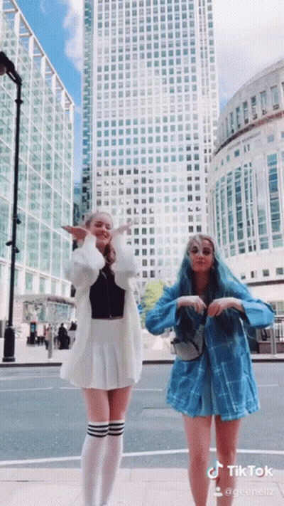 Two Girls Are Dancing In Front Of A Tall Building And A Sign That Says Tiktok On It GIF