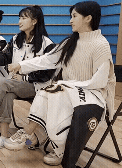 Two Girls Are Sitting In Chairs With One Wearing A Jacket That Says Twice GIF
