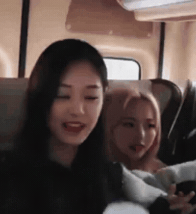 Two Girls Are Sitting Next To Each Other On A Bus And One Of Them Is Holding A Cell Phone . GIF