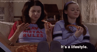Two Girls Are Sitting On A Couch Eating Pizza And One Has A Shirt That Says " Raw Metal Rules " GIF