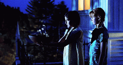 Two Girls Are Standing In Front Of A House At Night And One Is Holding A Bowl GIF