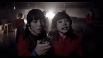 Two Girls In Red Jackets Standing In Dark Room GIF