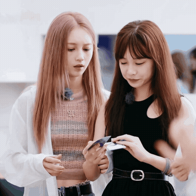 Two Girls Looking At Phone With Letter G On Belt GIF