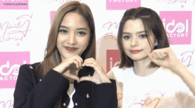 Two Girls Making Heart Shape In Front Of Idol Factory Sign GIF