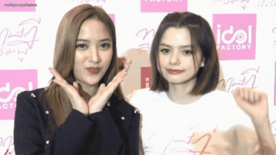 Two Girls Posing In Front Of Idol Factory Sign GIF