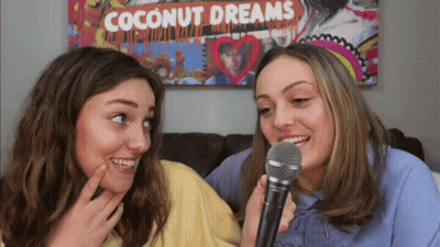 Two Girls Singing Into Microphones In Front Of Coconut Dreams Poster GIF