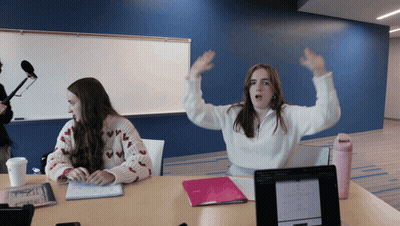 Two Girls Sitting At Table With Arms Up GIF