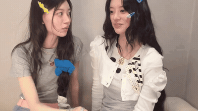 Two Girls Sitting Next To Each Other With Necklace Saying A GIF