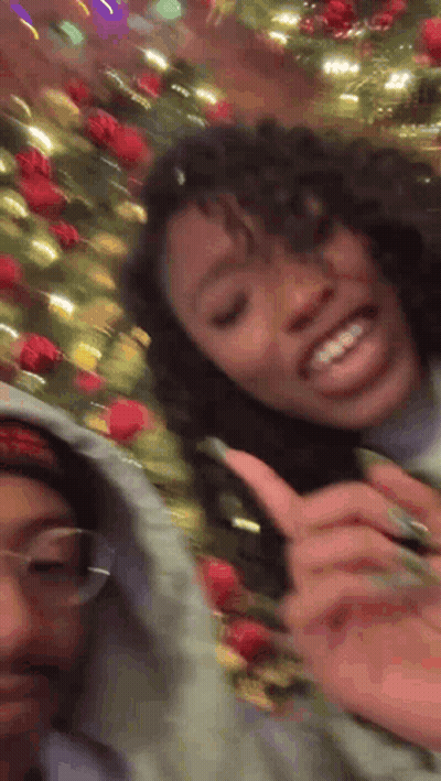 Two Girls Smiling Next To Christmas Tree GIF