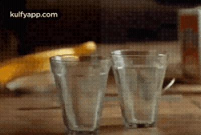 Two Glasses Of Water Are Sitting On A Wooden Table With A Banana In The Background . GIF