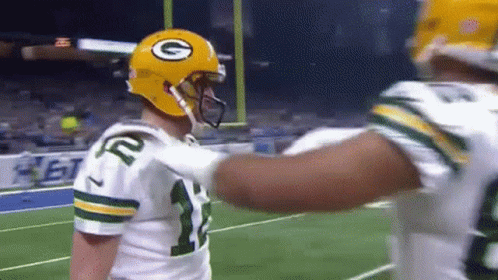 Two Green Bay Packers Players Are Hugging Each Other On A Football Field . GIF