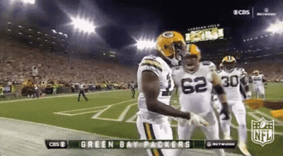 Two Green Bay Packers Players Are Hugging Each Other On The Field During A Football Game . GIF