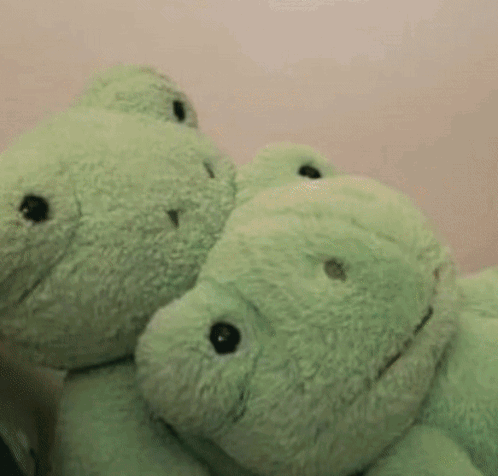 Two Green Teddy Bears Are Hugging Each Other Against A Pink Wall GIF