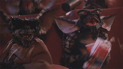 Two Gremlins Sitting In Theater One Holding Chips GIF
