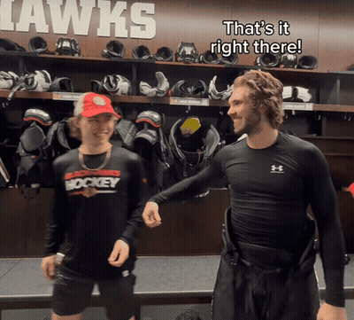 Two Hockey Players In A Locker Room That Says Hawks On The Wall Behind Them GIF
