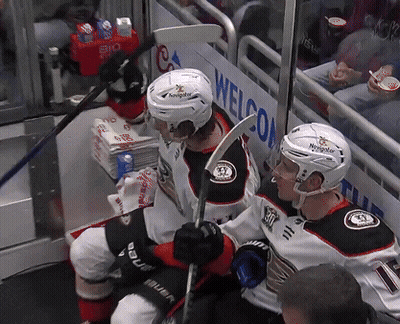 Two Hockey Players Sitting In Front Of A Sign That Says Welcom GIF