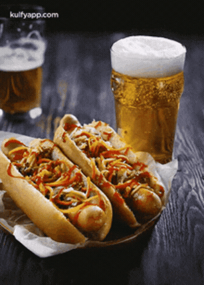 Two Hot Dogs Sit Next To A Glass Of Beer GIF