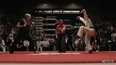Two Karate Fighters Are Fighting In Front Of An All Valley Karate Championship Sign GIF