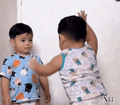 Two Little Boys Are Standing Next To Each Other And One Of Them Is Reaching For The Other 'S Arm . GIF
