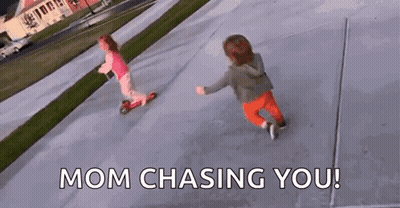 Two Little Girls Are Riding Scooters On A Sidewalk And The Words `` Mom Chasing You '' Are Visible . GIF