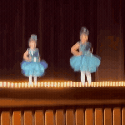 Two Little Girls In Blue Dresses Are Dancing On A Stage . GIF