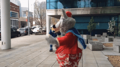 Two Mascots Dancing In Front Of Downtown Building GIF