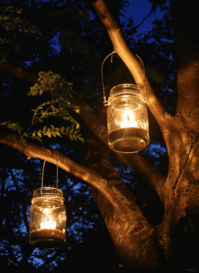 Two Mason Jars With Candles Hanging From Tree GIF