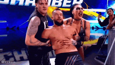 Two Men And A Woman Are Holding A Shirtless Wrestler In A Ring . GIF