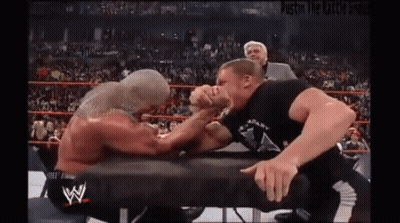 Two Men Are Arm Wrestling In A Wrestling Ring With A Referee Watching . GIF