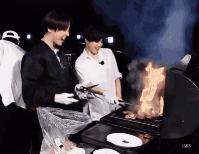Two Men Are Cooking Food On A Grill While Another Man Watches . GIF