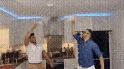 Two Men Are Dancing In A Kitchen In Front Of A Fire Alarm . GIF