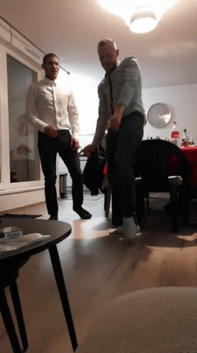 Two Men Are Dancing In A Living Room With A Bottle Of Coca Cola Behind Them GIF