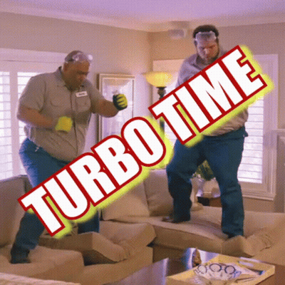Two Men Are Dancing In A Living Room With Turbo Time Written On The Sign GIF