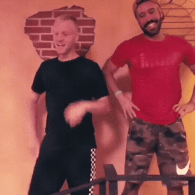 Two Men Are Dancing In A Room With A Brick Wall In The Background . GIF